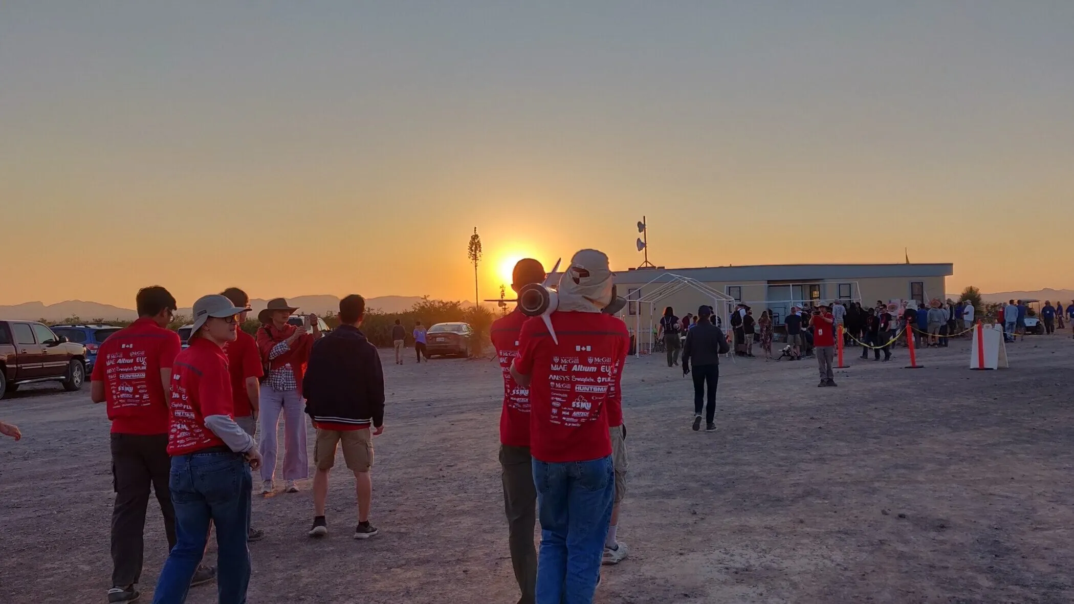A person carrying a rocket into the sunset on a desert test-site.